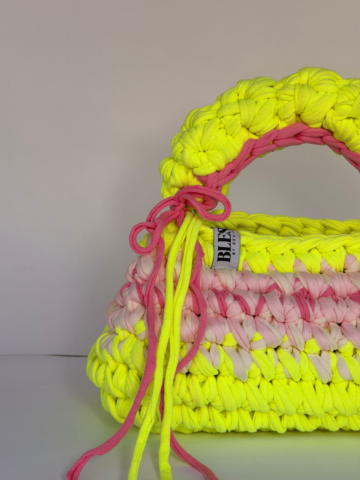 Neon yellow bobble-stitch crochet bag banded with blush, with a chunky top handle and bows