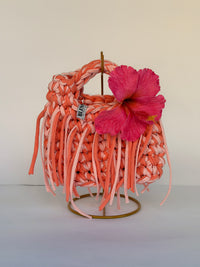 Coral and blush crochet bag with a braided top handle, long fringe and a pink hibiscus flower