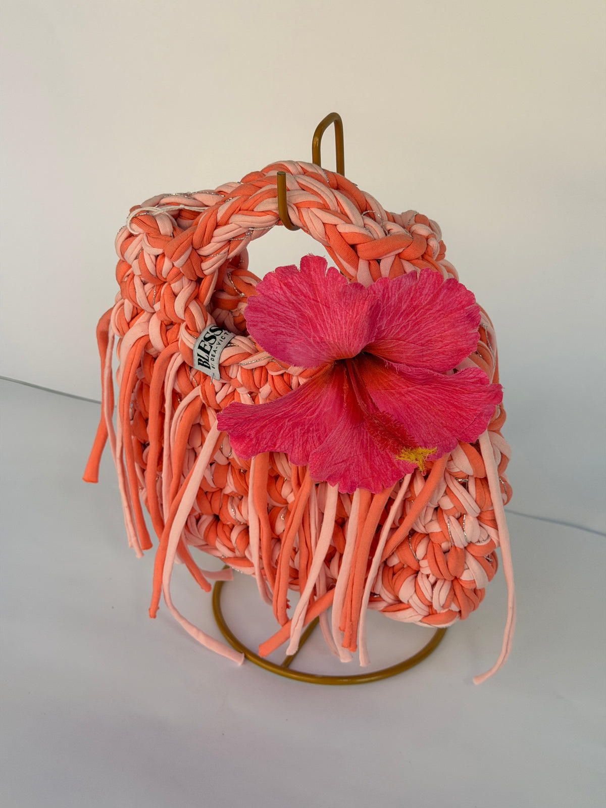 Coral and blush crochet bag with a braided top handle, long fringe and a pink hibiscus flower
