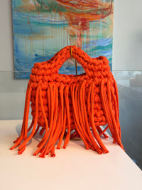 Bright orange crochet bag with a chunky braided top handle and a long fringe