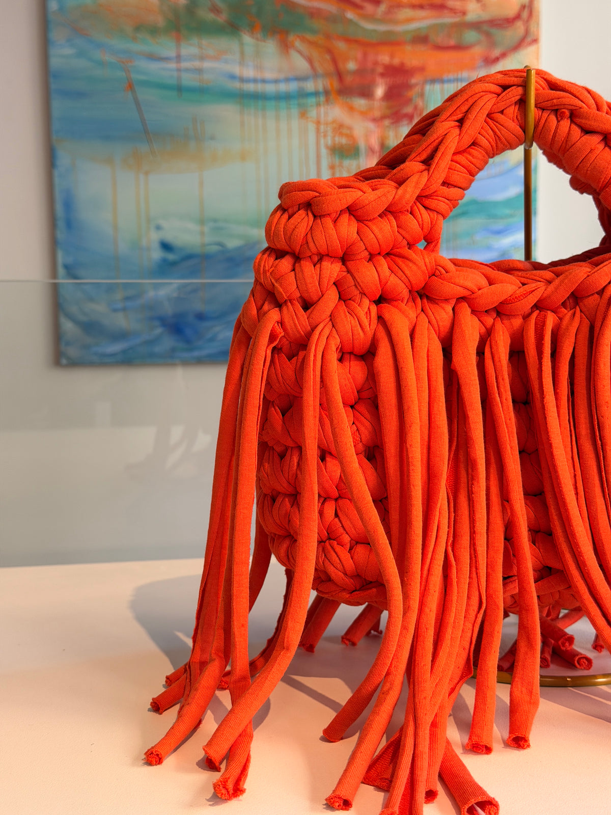 Bright orange crochet bag with a chunky braided top handle and a long fringe