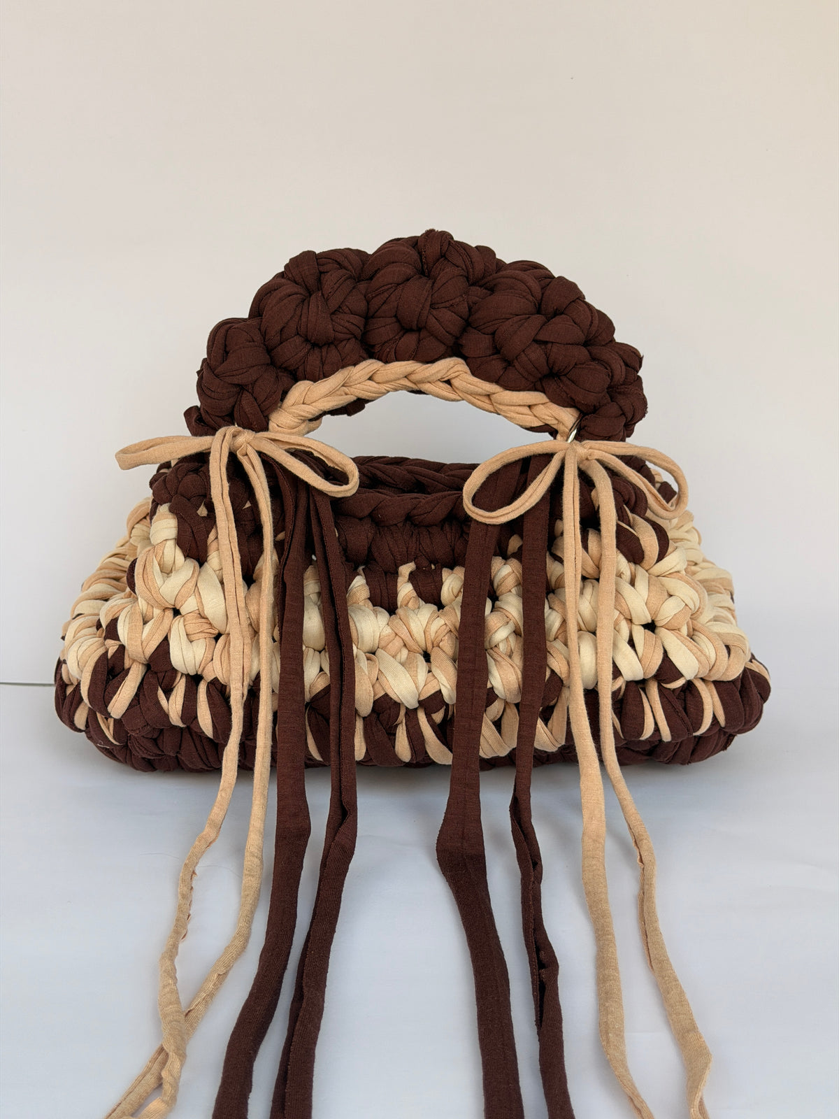 Brown and cream crochet bag with a braided top handle and long ties tied in bows