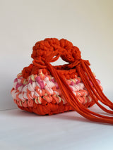 Side view of an orange and pink crochet bag in a deep bobble stitch with long orange ties