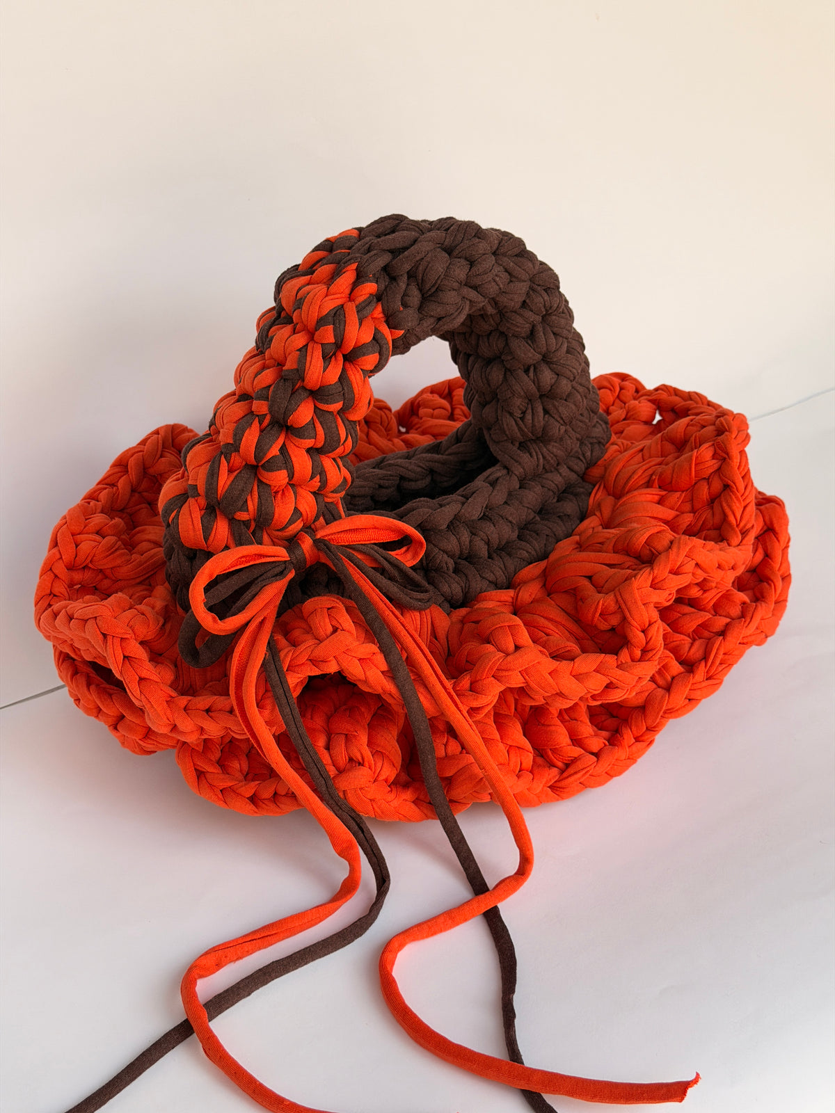 Close view of the two arc handles on a bright orange and brown crochet bag with a bow tied at the base