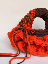 Top view of a bright orange crochet bag showing the brown handle and the orange and brown plaited handle