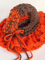 Bright orange crochet bag with a deep brown collar, two arc handles and long orange and brown ties