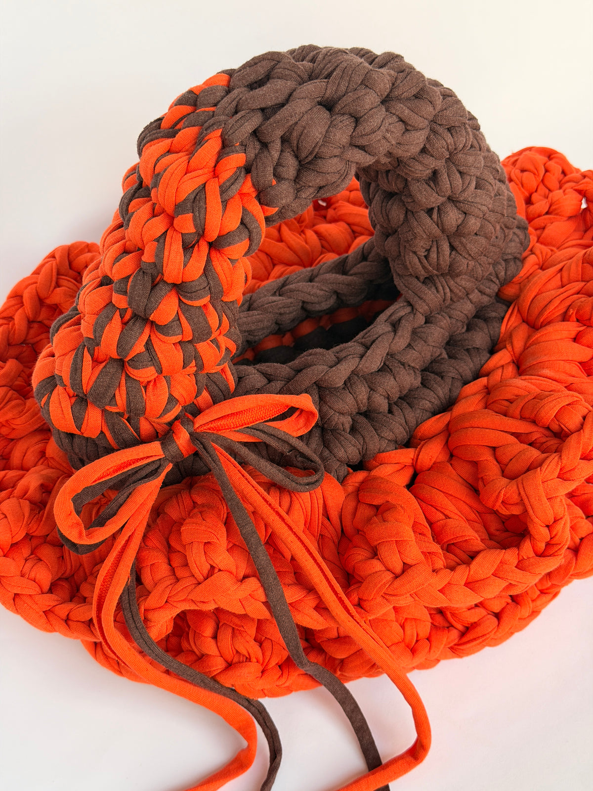 Bright orange crochet bag with a deep brown collar, two arc handles and long orange and brown ties
