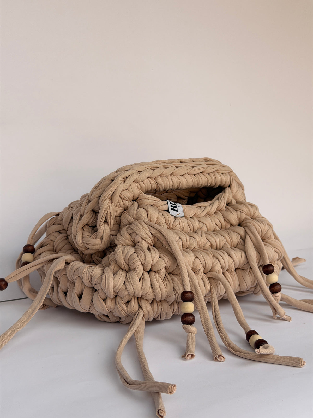 Side view of a sand coloured crochet clutch with beaded ties falling around it