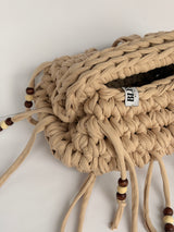 Close view of the braided top handle, woven Blessed label and wooden beads on a sand crochet clutch