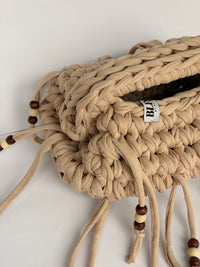 Close view of the braided top handle, woven Blessed label and wooden beads on a sand crochet clutch