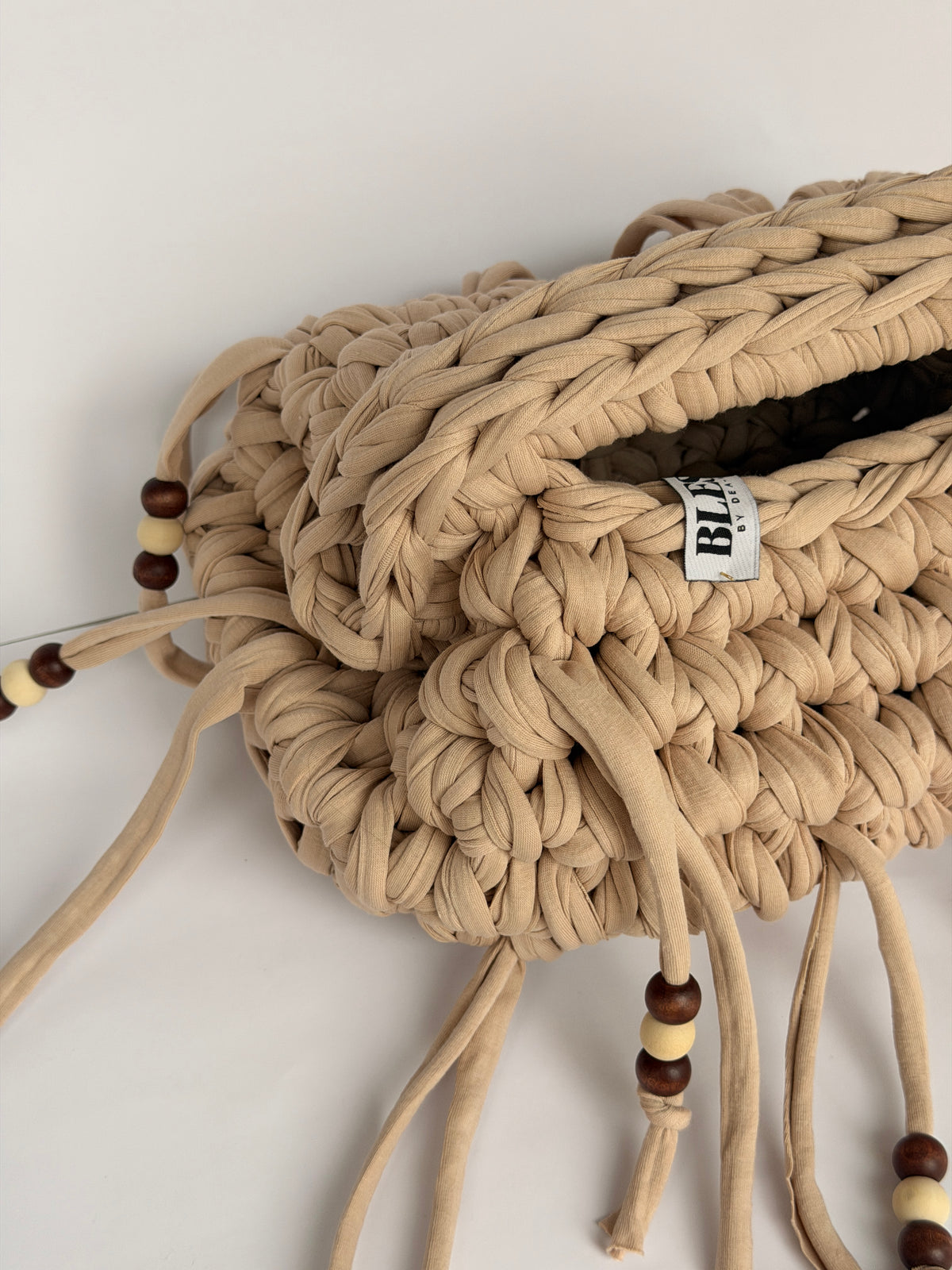 Close view of the braided top handle, woven Blessed label and wooden beads on a sand crochet clutch