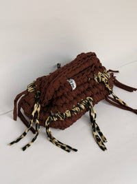 Top view of a warm brown crochet clutch with braided handle, woven Blessed label and leopard ties