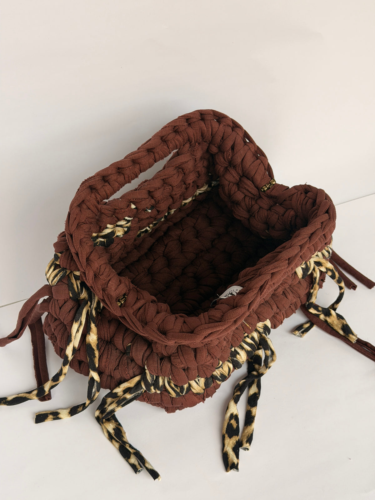 Warm brown crochet clutch with a leopard print band and leopard ties, woven Blessed label visible