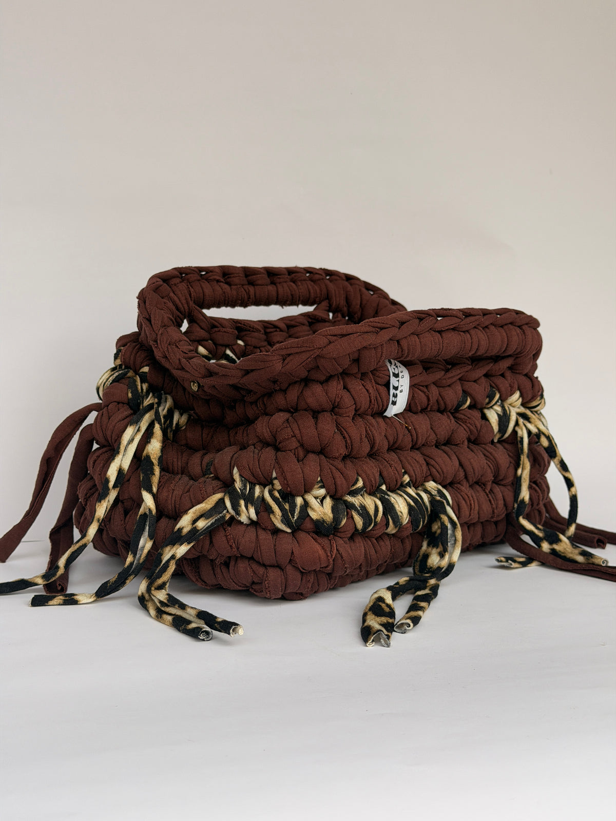 Open top of a warm brown crochet clutch with leopard print ties around the base
