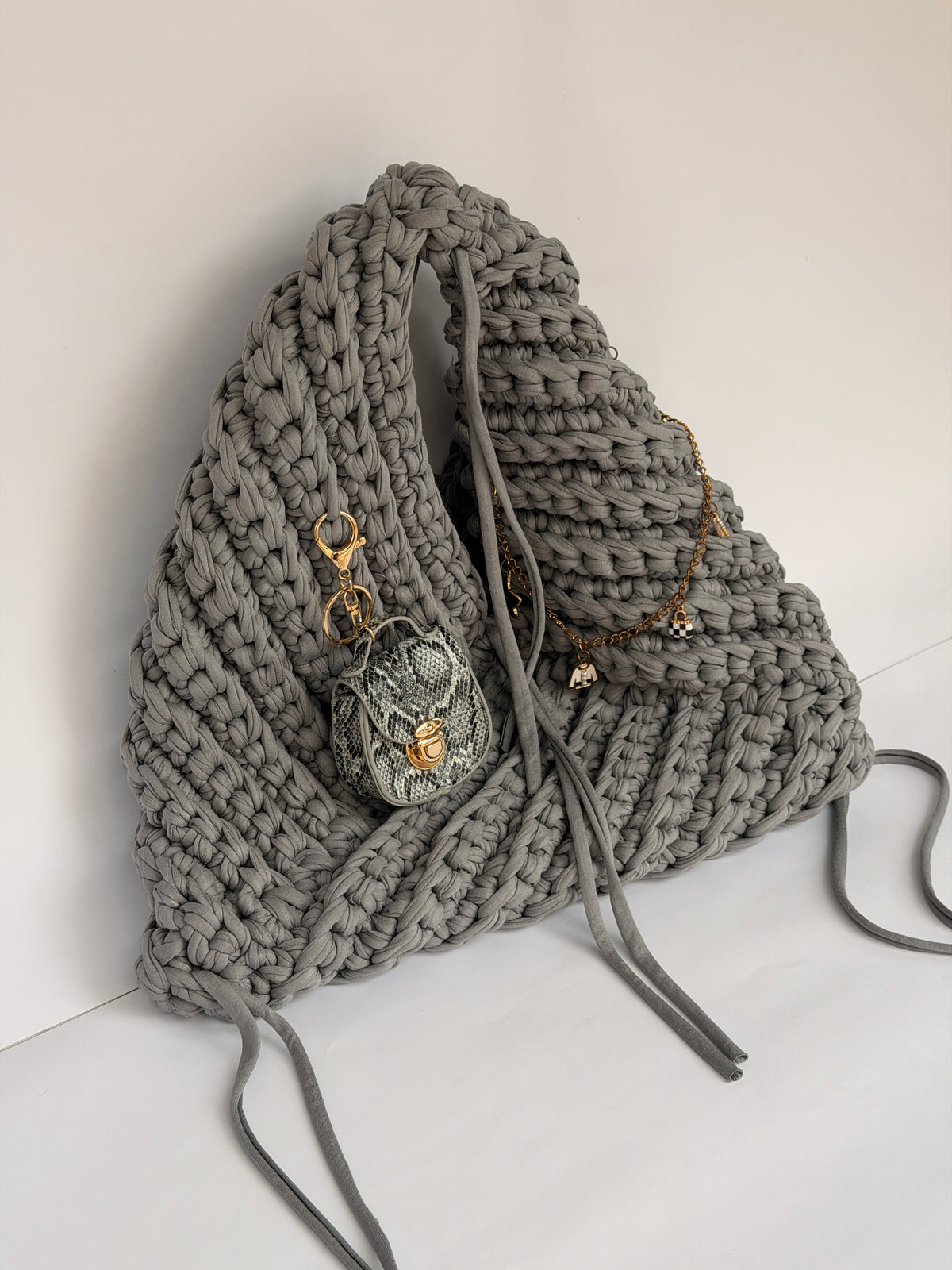 Close view of the snakeskin mini bag charm clipped to a grey crochet origami bag