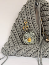Grey crochet origami bag knotted at the top, with a snakeskin mini bag charm and a gold charm chain