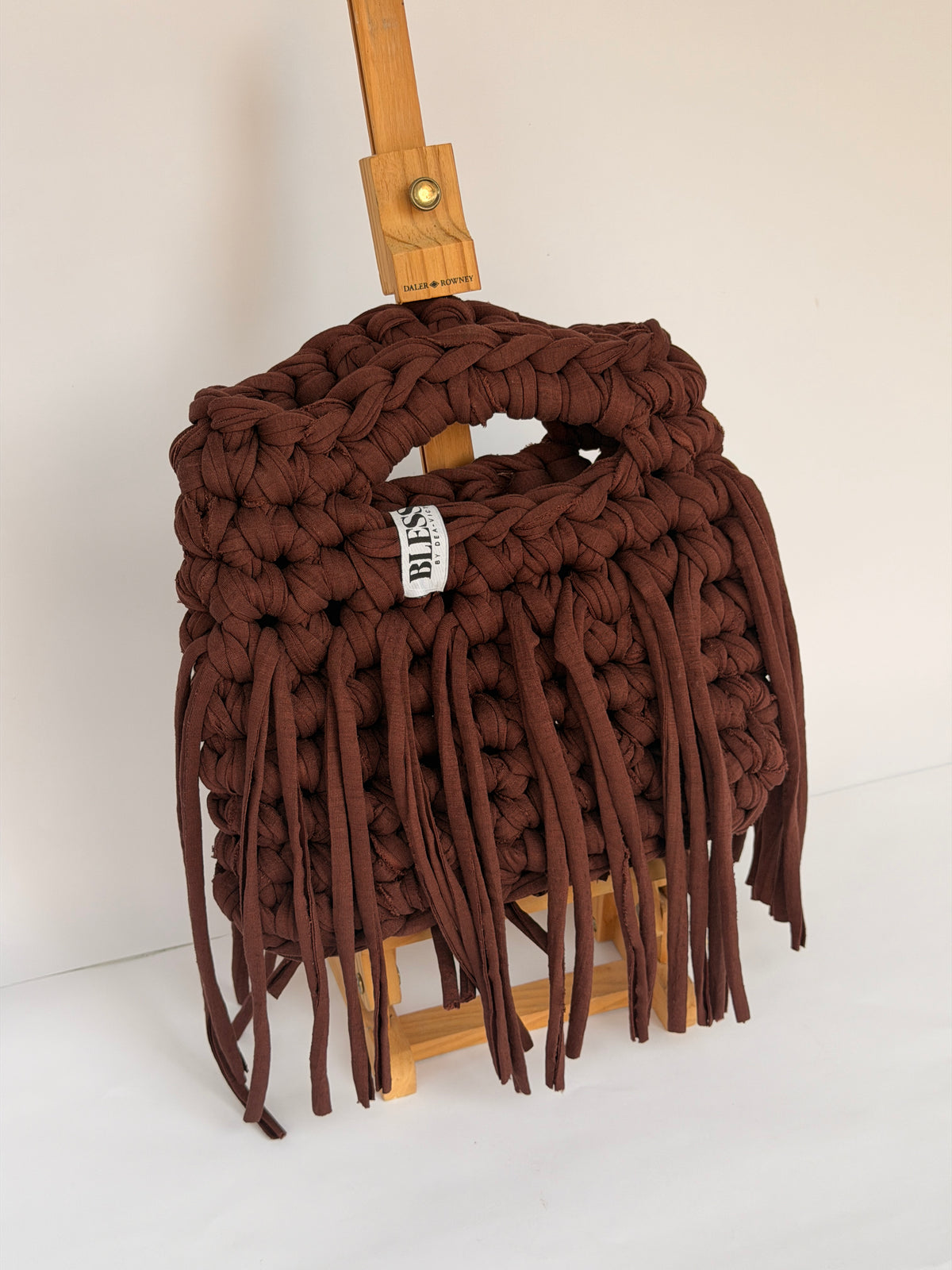 Deep brown crochet Sasha bag with a braided top handle, long fringe and woven Blessed label