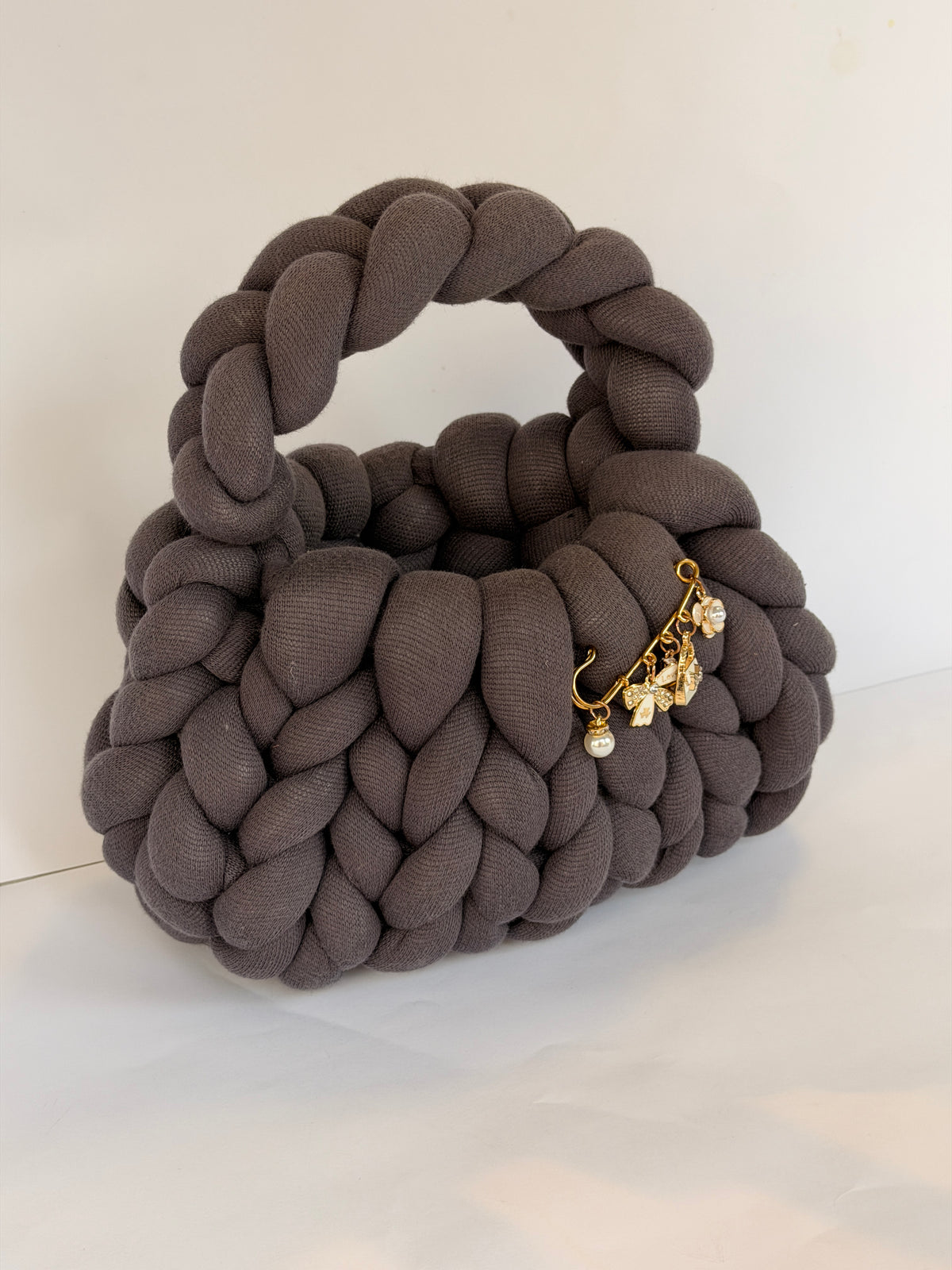 Charcoal grey chunky crochet bag with a braided top handle and a gold brooch with pearl, bow and flower charms