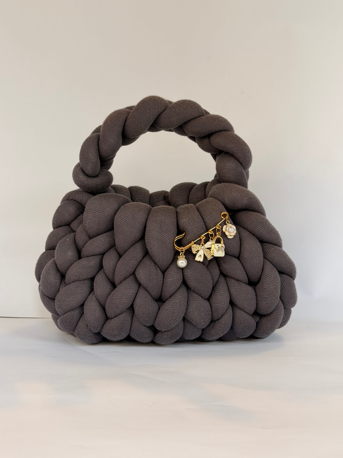 Top view of a charcoal grey chunky crochet bag with a gold charm brooch on the rim