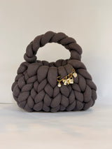 Top view of a charcoal grey chunky crochet bag with a gold charm brooch on the rim