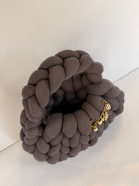 Angled view of a charcoal grey crochet bag in jumbo yarn with a gold charm brooch