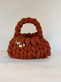 Close view of the gold charm brooch on a rust chunky crochet bag