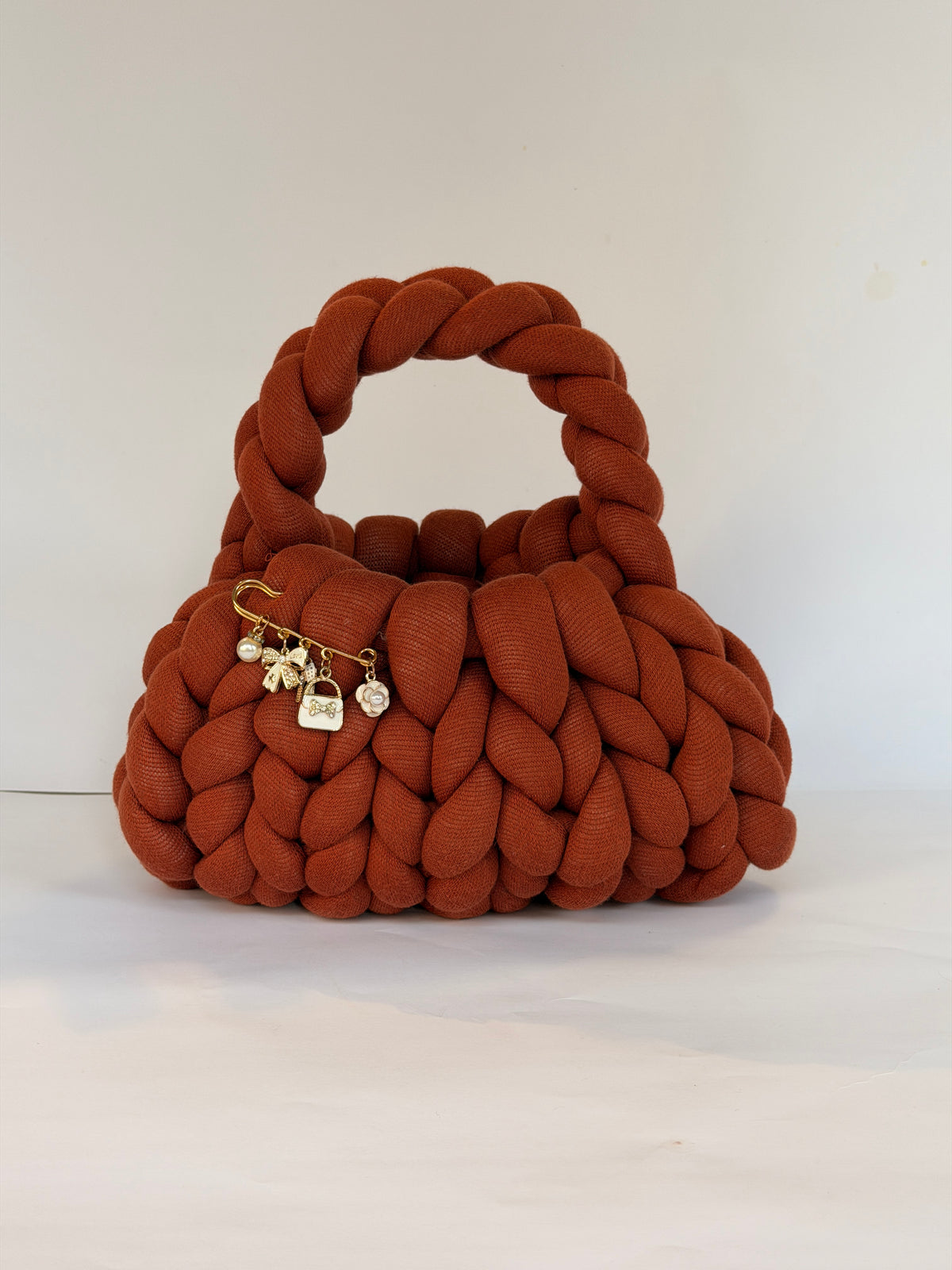 Close view of the gold charm brooch on a rust chunky crochet bag