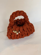 Angled view of a rust crochet bag in jumbo yarn with a gold brooch of pearl, bow and flower charms