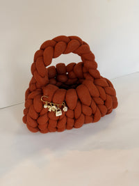 Angled view of a rust crochet bag in jumbo yarn with a gold brooch of pearl, bow and flower charms