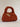 Rust orange chunky crochet bag with a braided top handle and a gold charm brooch