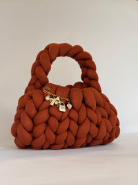 Rust orange chunky crochet bag with a braided top handle and a gold charm brooch