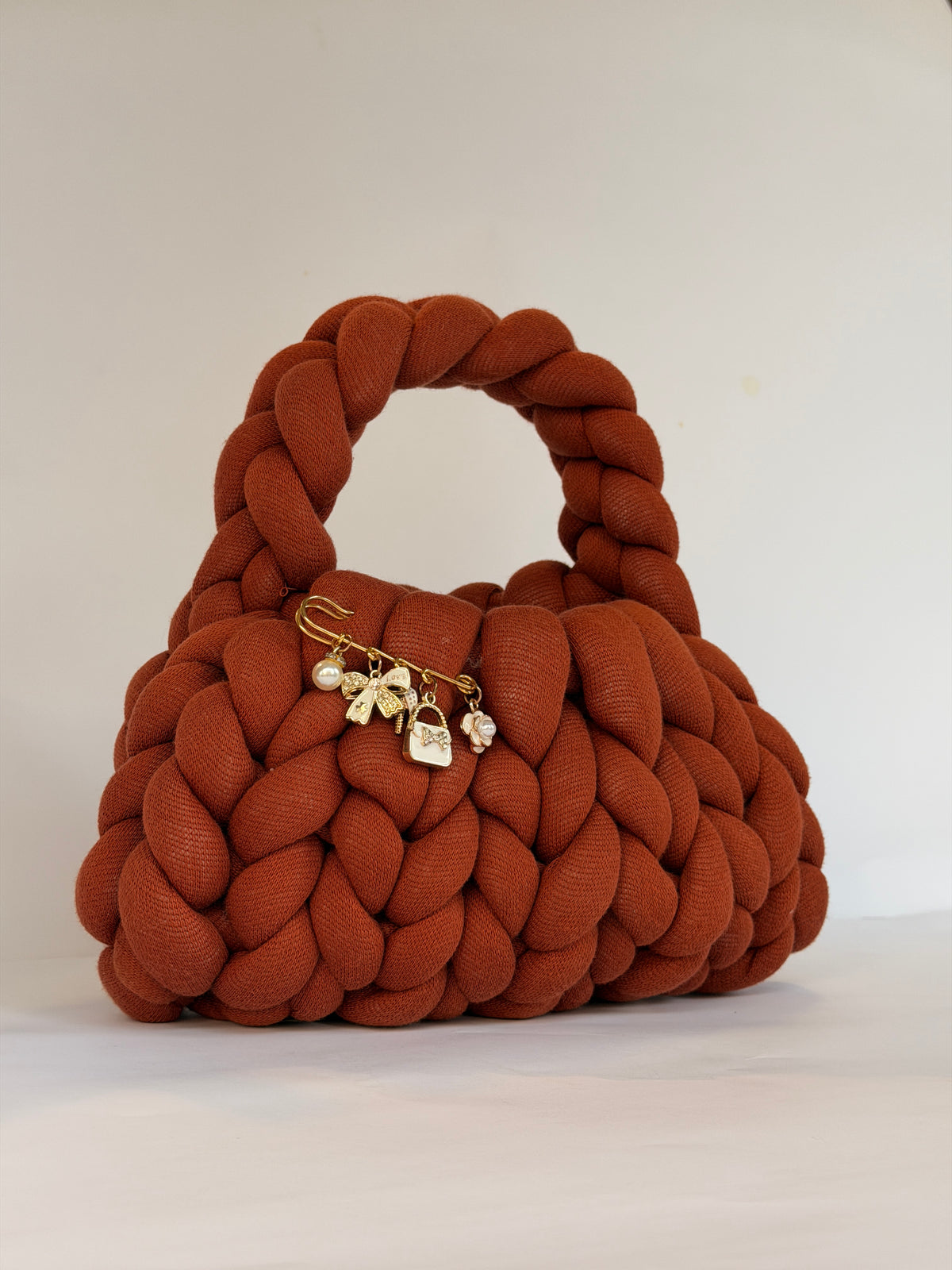 Rust orange chunky crochet bag with a braided top handle and a gold charm brooch