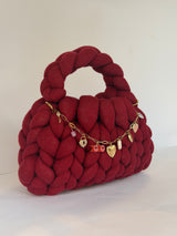 Side view of a deep red chunky crochet bag with an XOXO and heart locket charm chain
