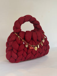 Side view of a deep red chunky crochet bag with an XOXO and heart locket charm chain