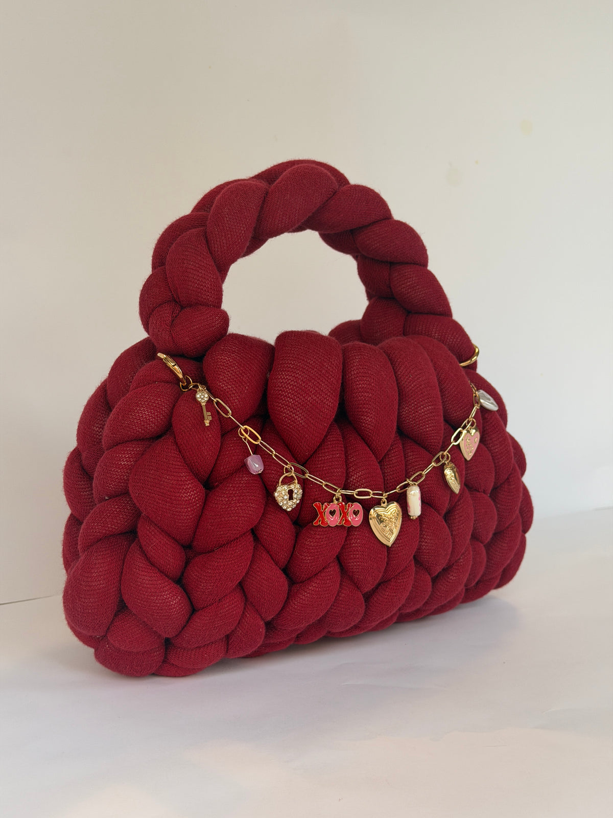 Side view of a deep red chunky crochet bag with an XOXO and heart locket charm chain