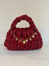 Angled view of a deep red crochet bag in jumbo yarn with a gold chain of heart, key and padlock charms