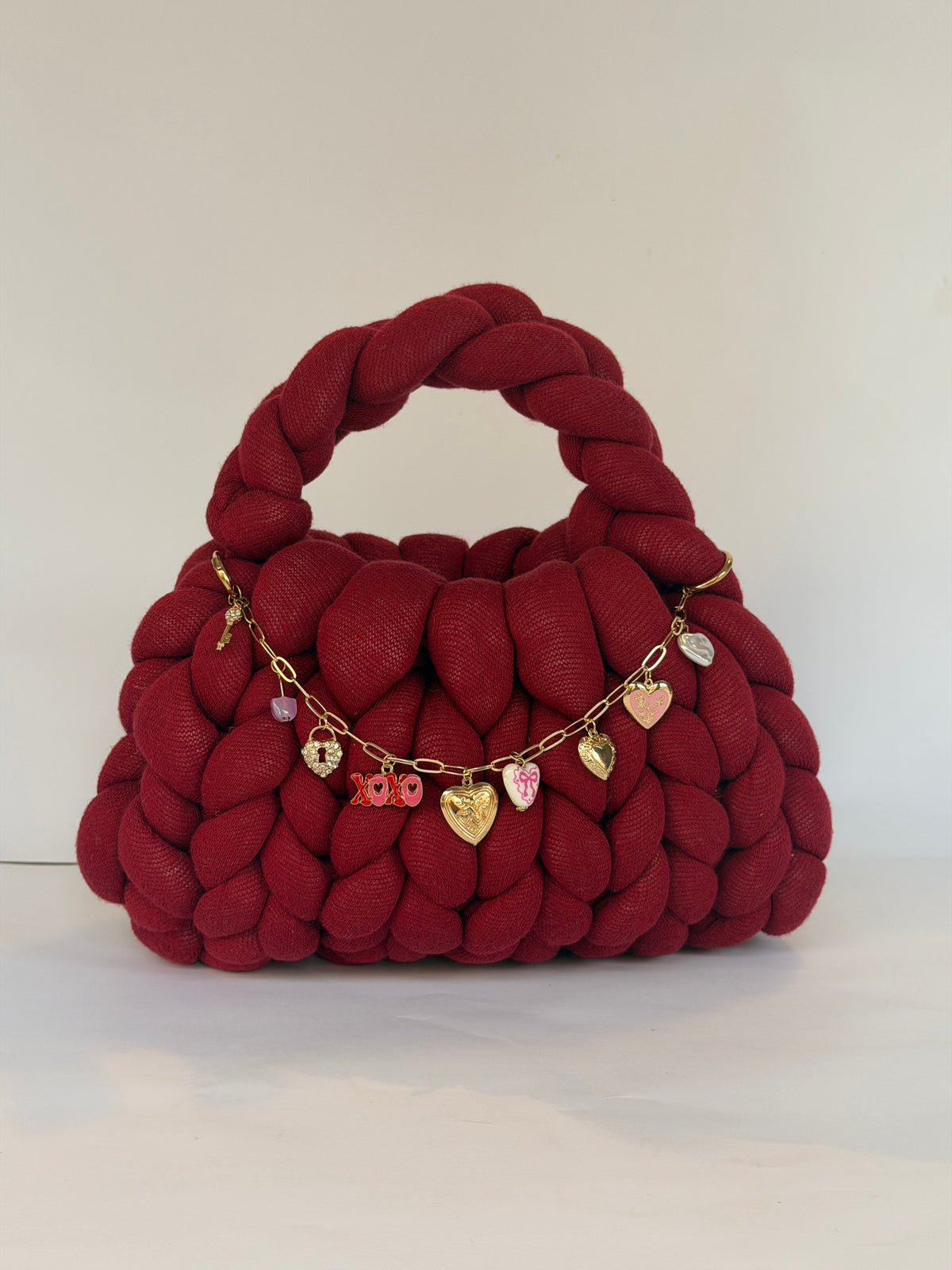 Angled view of a deep red crochet bag in jumbo yarn with a gold chain of heart, key and padlock charms