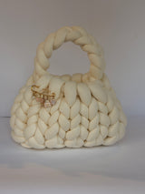 Cream chunky crochet bag with a braided top handle and a gold brooch of pearl, bow and flower charms