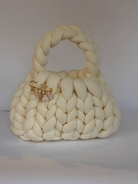 Cream chunky crochet bag with a braided top handle and a gold brooch of pearl, bow and flower charms