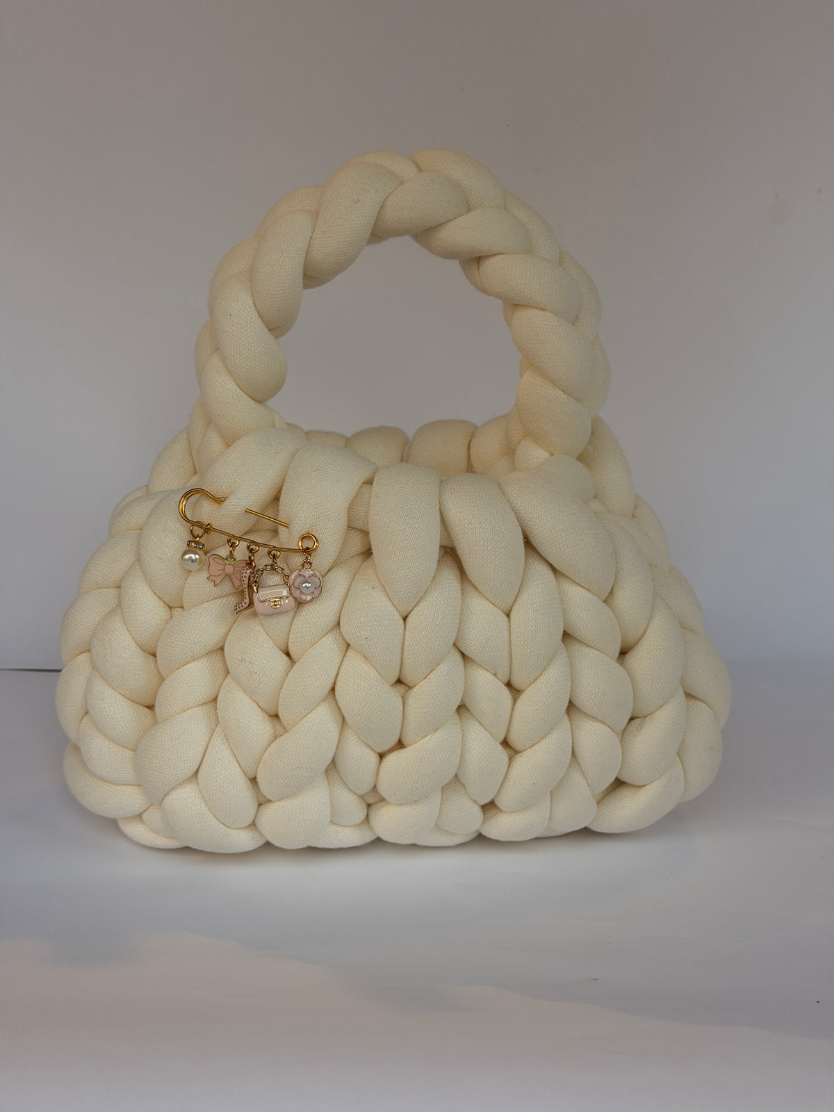 Cream chunky crochet bag with a braided top handle and a gold brooch of pearl, bow and flower charms