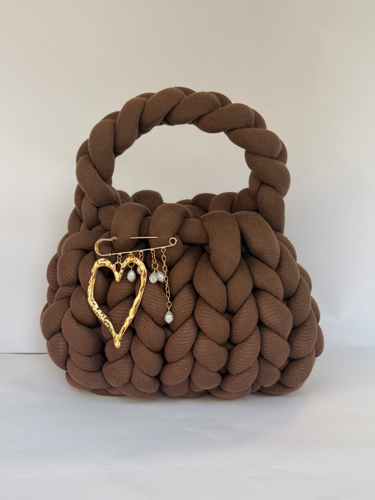 Gold hammered heart brooch with pearl drops pinned to a chunky brown crochet bag