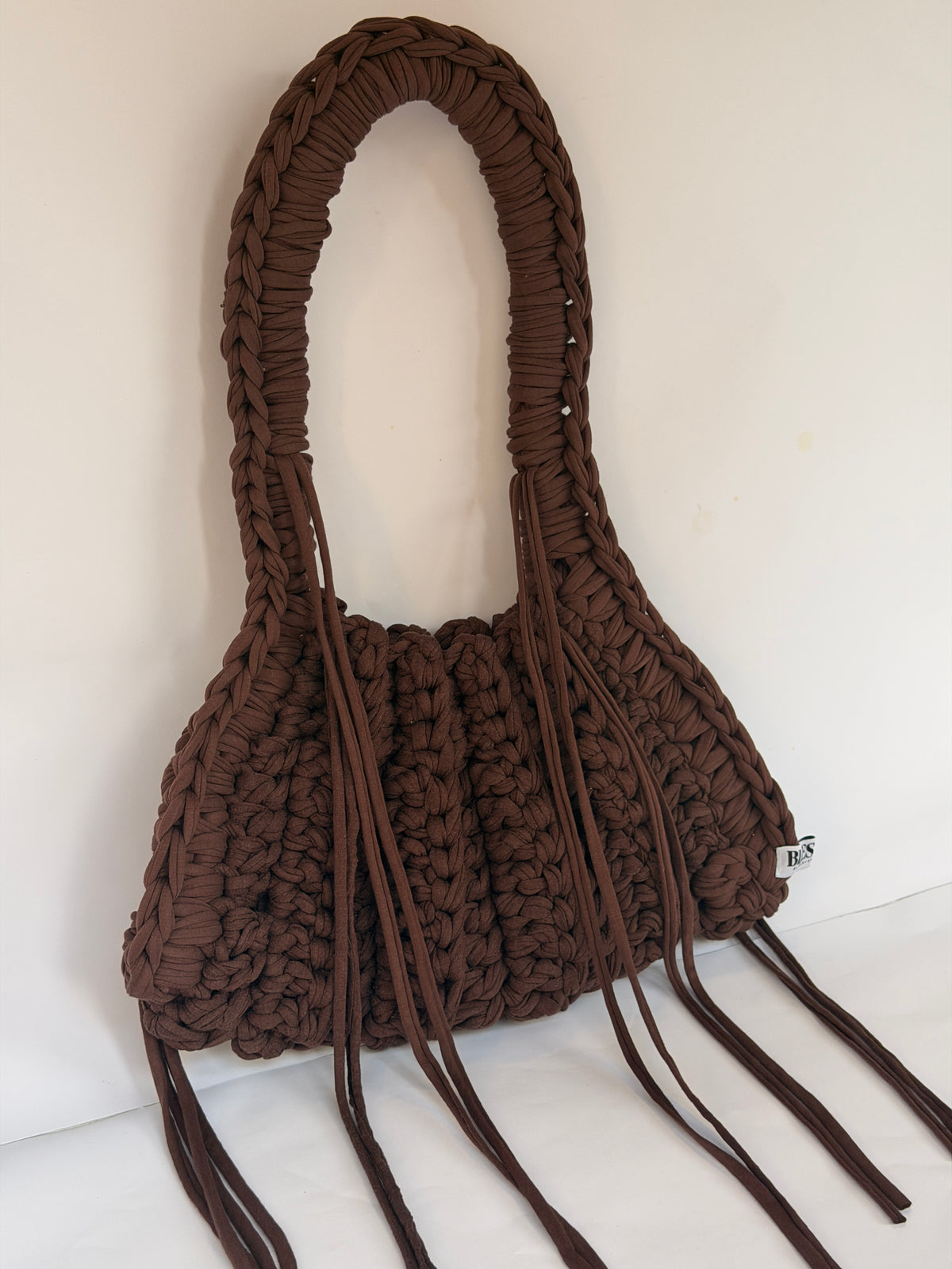 Front view of a deep brown ribbed crochet shoulder bag with long ties falling past the base