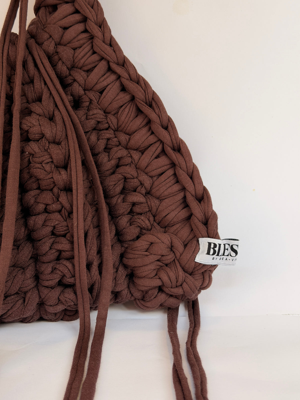 Angled view of a deep brown crochet shoulder bag with a wrapped braided handle