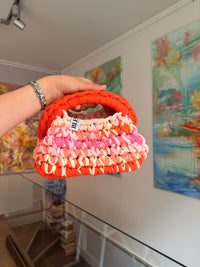 Bright orange crochet clutch with a peach, pink and cream fringe