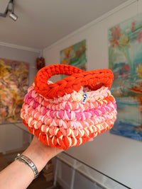 Bright orange crochet clutch with a peach, pink and cream fringe