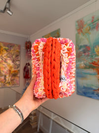 Bright orange crochet clutch with a peach, pink and cream fringe