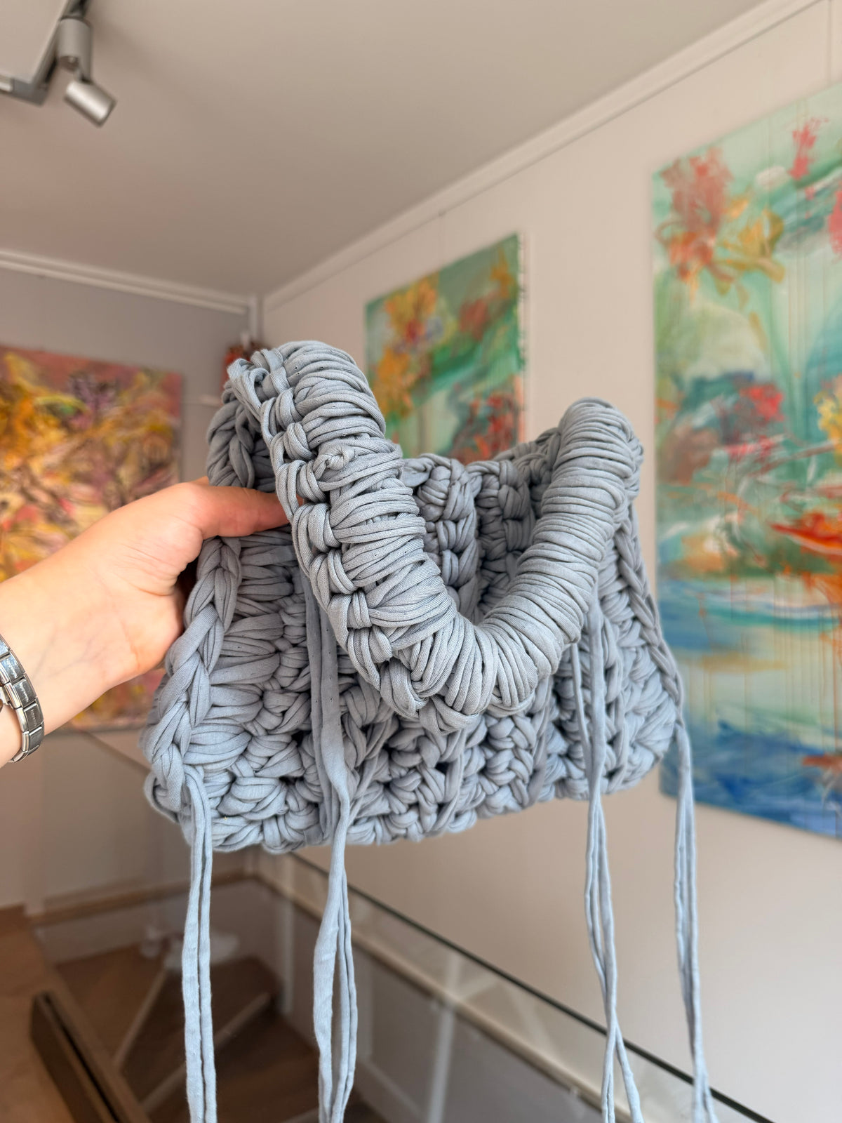 Pale grey crochet shoulder bag hanging, full length with side ties