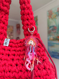 Bright red crochet bag with a wide top handle, long ties and a beaded jellyfish charm