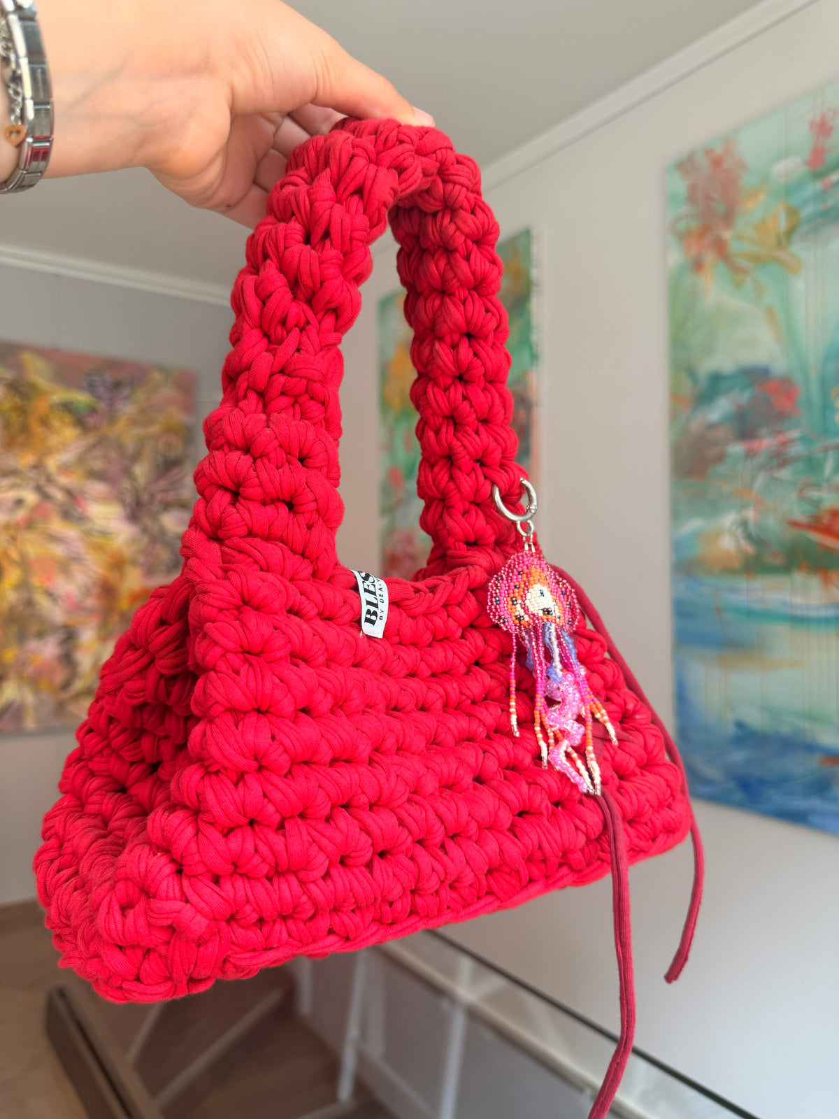Bright red crochet bag with a wide top handle, long ties and a beaded jellyfish charm