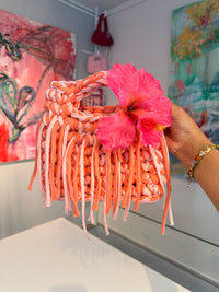 Coral and blush crochet bag with a braided top handle, long fringe and a pink hibiscus flower